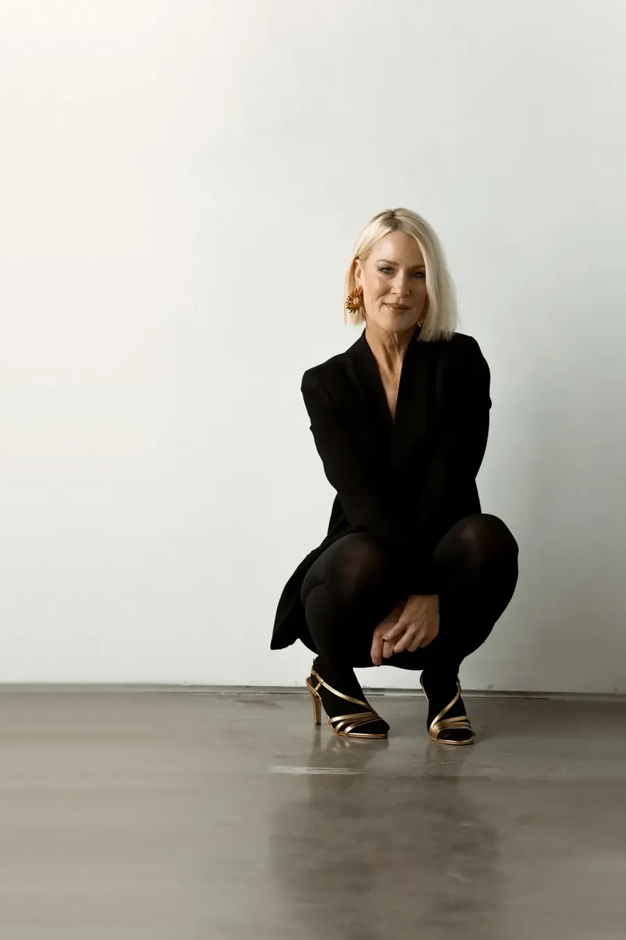 Amy Kurtz, platinum bob and black blazer, against a white studio wall